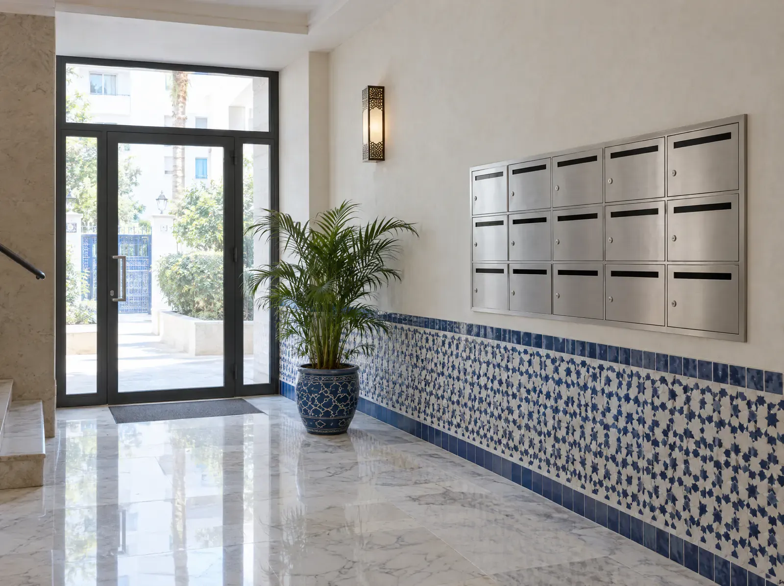 Hall d’immeuble au sol de marbre, avec une rangée de boîtes aux lettres et une frise de zellige